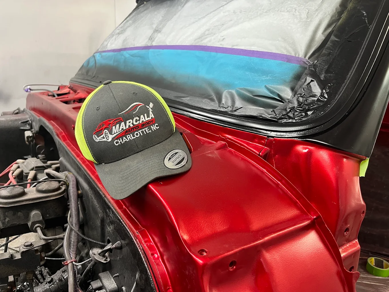 A Marcala Auto Body shop cap resting on a freshly painted red fender inside the booth